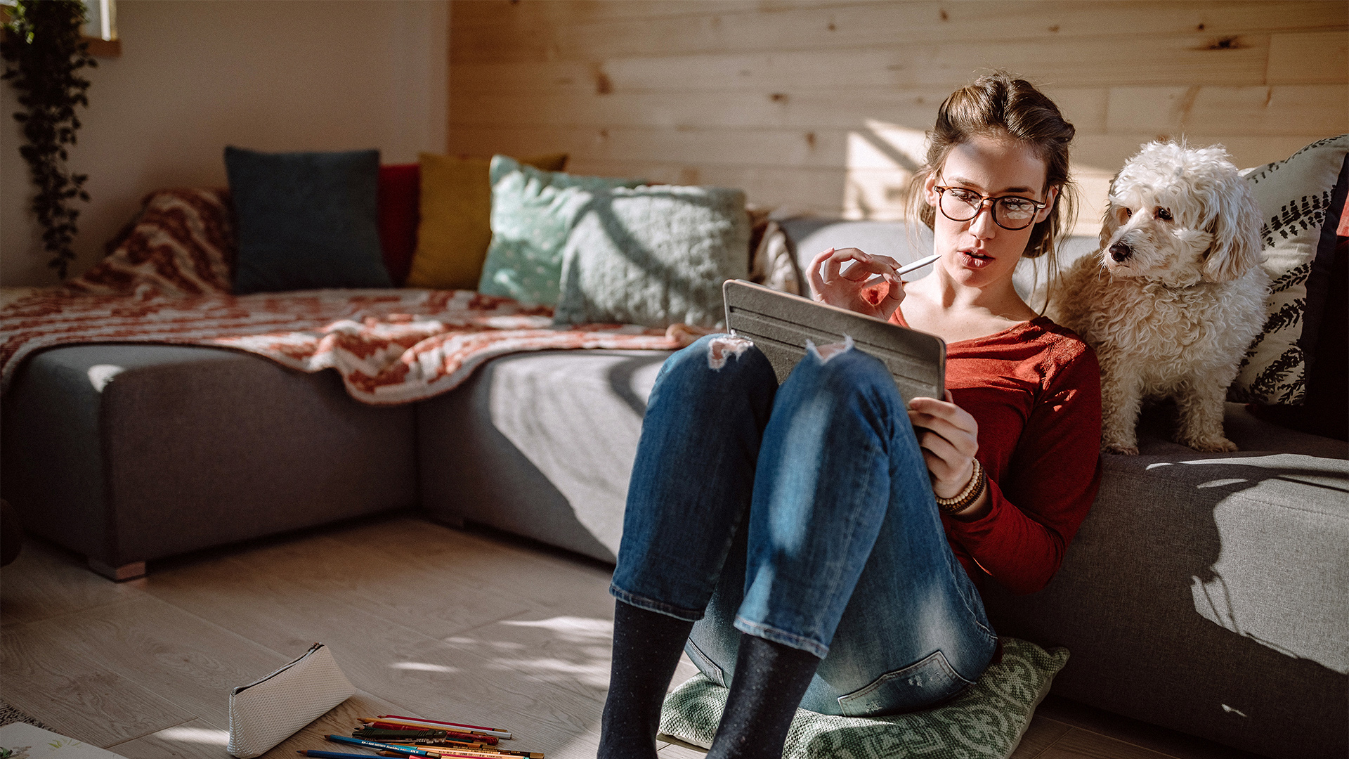 Woman in a living room with a tablet and a dog looking over her shoulder